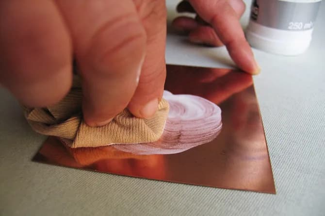 A closer view of the same cleaning: the cloth bunched under a thumb, the paste spread in a broad arc across the copper.