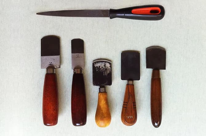 Five mezzotint rockers with turned wooden handles laid in a row below a flat steel file, the toothed blades varying in width.