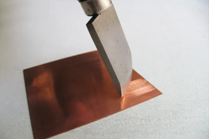 A rocker held upright against the copper, its toothed edge biting a band of texture into the plate.